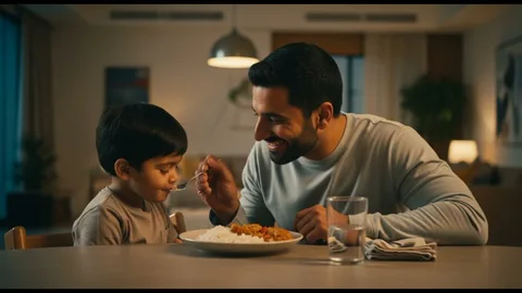 A father smiling as he feeds his young son at the dinner table